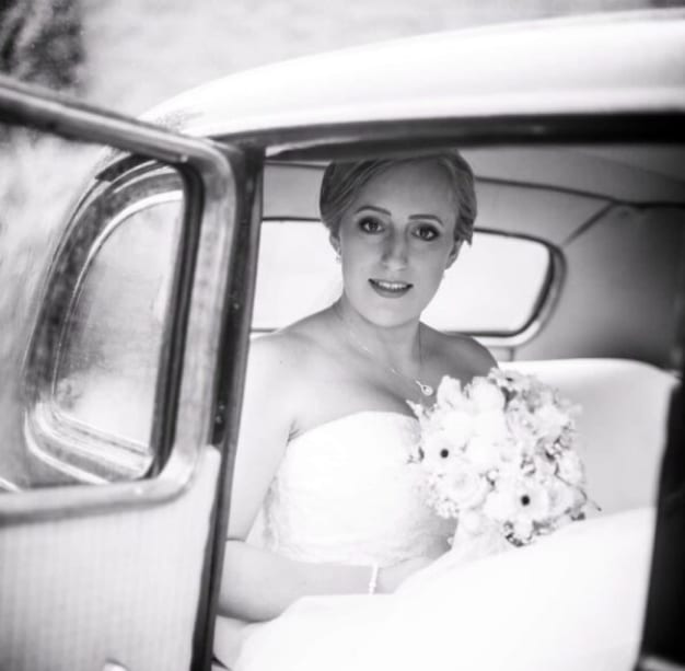 eine gestylte Braut mit Blumen in der Hand, sitzend im Auto